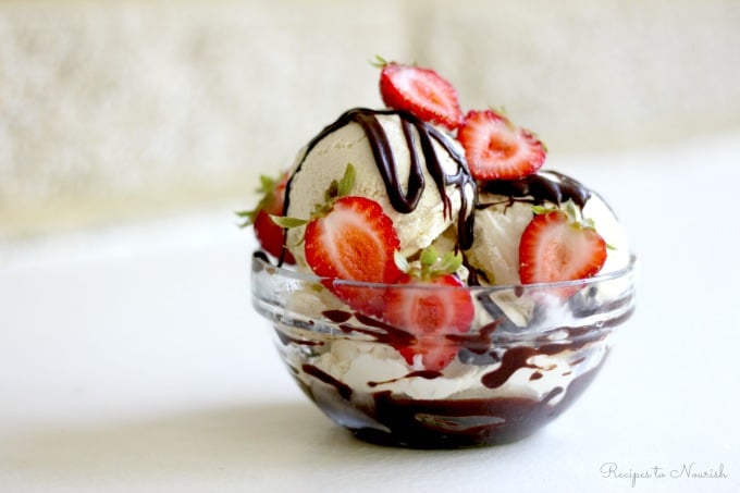 Bowl of vanilla ice cream topped with fresh strawberries and chocolate fudge sauce.