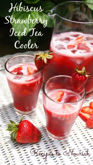 Hibiscus strawberry herbal iced tea in glasses and a pitcher with fresh strawberries.