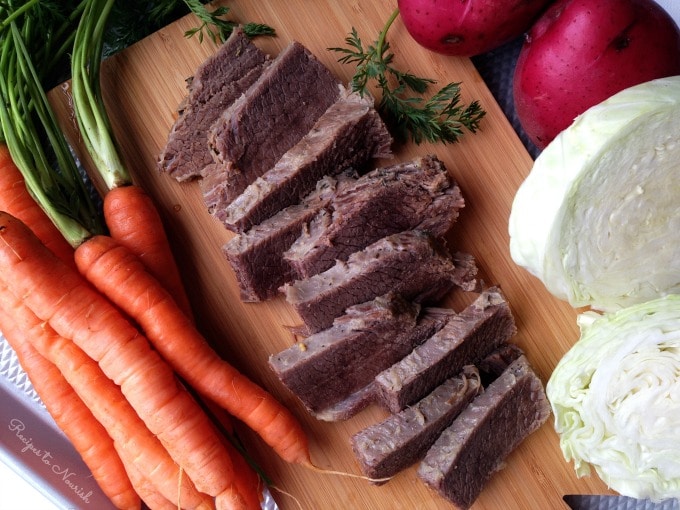 Slices of corned beef on a cutting board with carrots, cabbage and red potatoes.