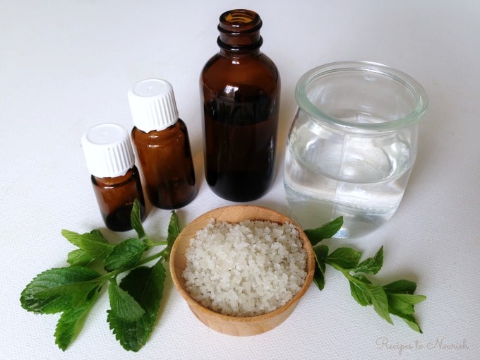 Amber essential oil bottles, a small glass of water, sea salt and fresh herbs.