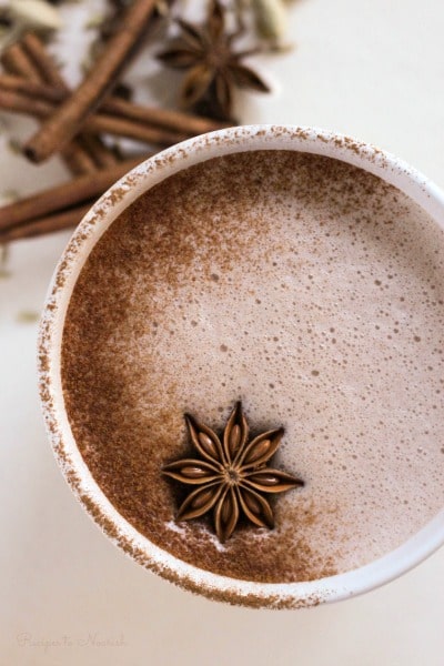 Hot chocolate with ground cinnamon and a star anise pod on top surrounded by chai spices.