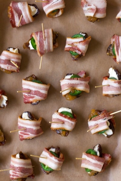 Stuffed bacon wrapped dates with cream cheese and jalapeño slices on a baking sheet.