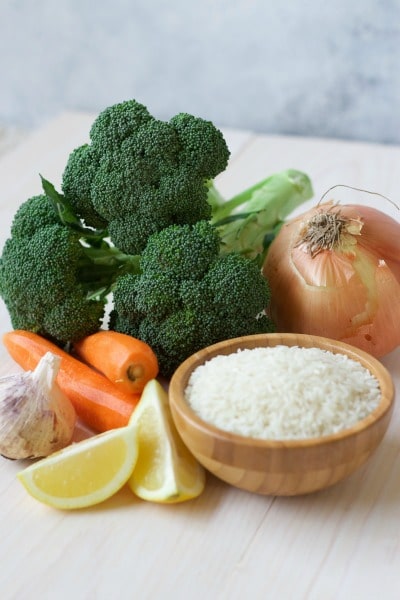 Fresh broccoli, carrots, onion, garlic, lemon and a bowl of white rice. 