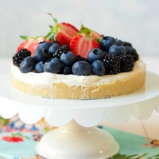 Cheesecake tart topped with fresh blueberries, strawberries and blackberries sitting on a cake stand.