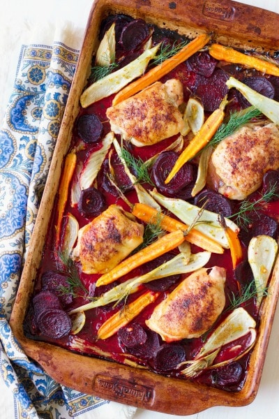 Roasted chicken thighs on a pan with roasted beets, carrots and fennel.