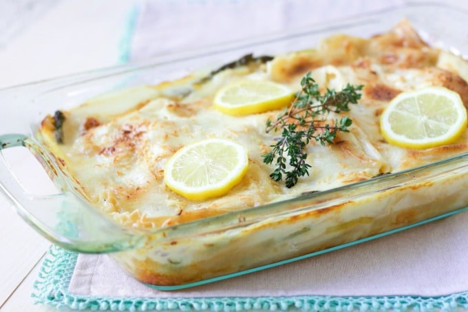 Creamy white sauce lasagna in a casserole dish with cheesy topping, lemon slices and fresh thyme.