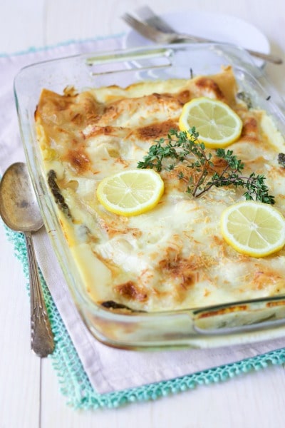 Creamy white sauce lasagna with cheesy topping with lemon slices, fresh thyme and serving utensils. 