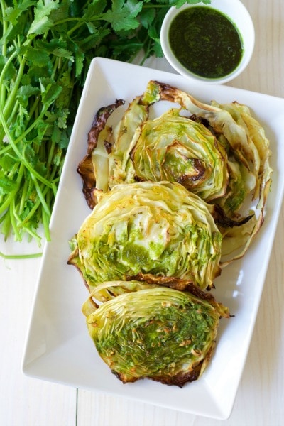 Roasted cabbage steaks with fresh cilantro and chimichurri on the side.