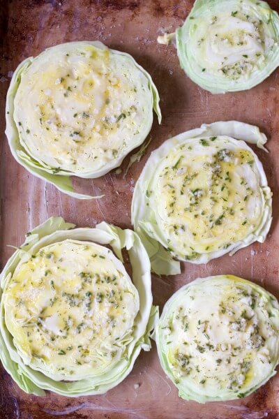 Raw cabbage steaks on a baking sheet with melted butter and herbs.