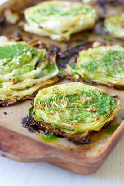 Roasted cabbage steaks on a baking sheet with chimichurri drizzled over the tops.