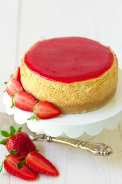 Whole cheesecake with strawberry sauce on the top and fresh strawberries around it.