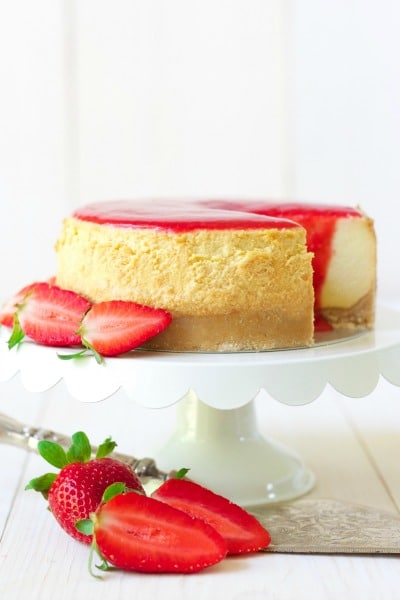 Whole cheesecake with a slice cut out and strawberry sauce on the top with fresh strawberries.