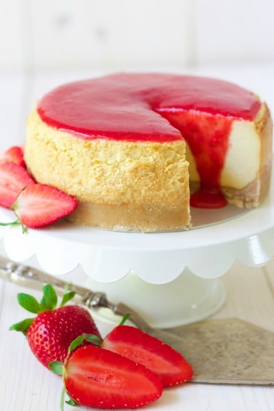 Cheesecake with a slice cut out and strawberry sauce on the top with fresh strawberries.