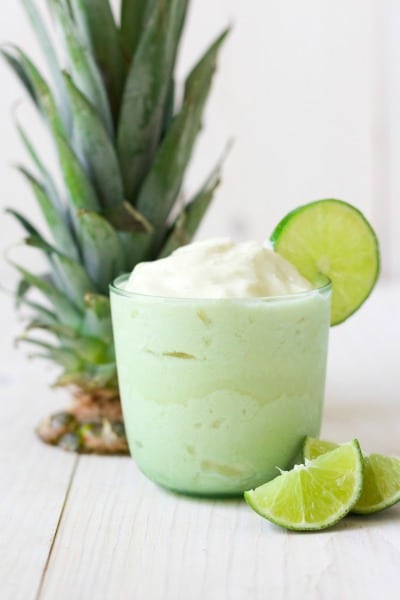 Glass of pineapple whip in a glass with fresh lime slices and pineapple top. 