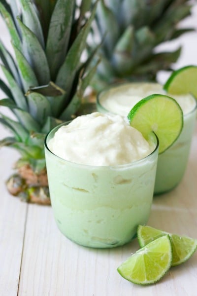 Two glasses of frozen pineapple whip with fresh lime slices and pineapple tops.