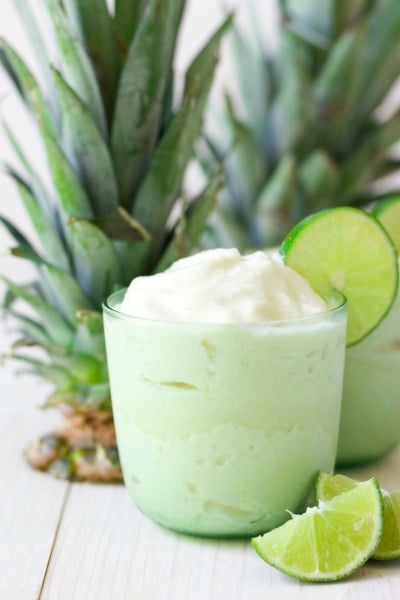 Two glasses of frozen pineapple whip with fresh limes slices and two pineapple tops.