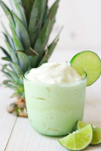 Glass of frozen pineapple whip with fresh lime slices and pineapple top.