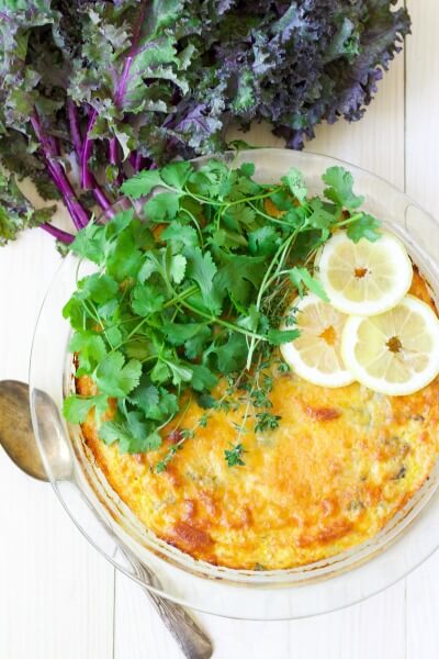 Breakfast casserole topped with fresh herbs and lemon slices surrounded by purple kale.