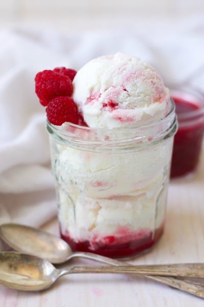 Scoops of raspberry swirl frozen yogurt in a jar with fresh raspberries and raspberry sauce.