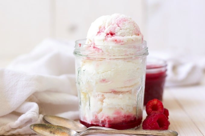 Scoops of raspberry swirl ice cream in a jar with raspberry sauce and fresh raspberries.