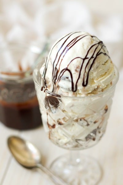 Ice cream in a glass with chocolate fudge sauce drizzled over the top and in a jar on the side.