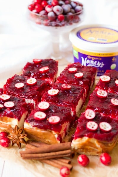 Slices of cranberry cheesecake bars with fresh cranberries and a container of Nancy's organic whole milk cottage cheese.