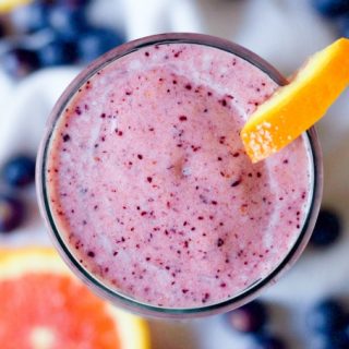 Pink smoothie in a glass with fresh blueberries and orange slices.