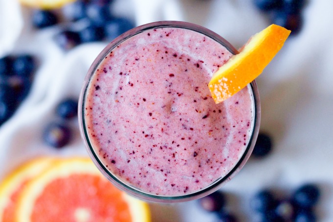 Pink smoothie in a glass with fresh blueberries and orange slices.
