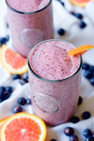 Two pink smoothies in glasses with fresh blueberries and orange slices.