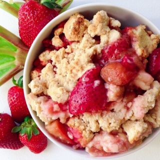 Fresh strawberries and rhubarb with a bowl of strawberry rhubarb cobbler.