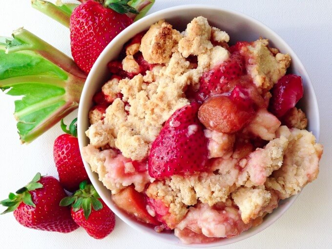 Fresh strawberries and rhubarb with a bowl of strawberry rhubarb cobbler.