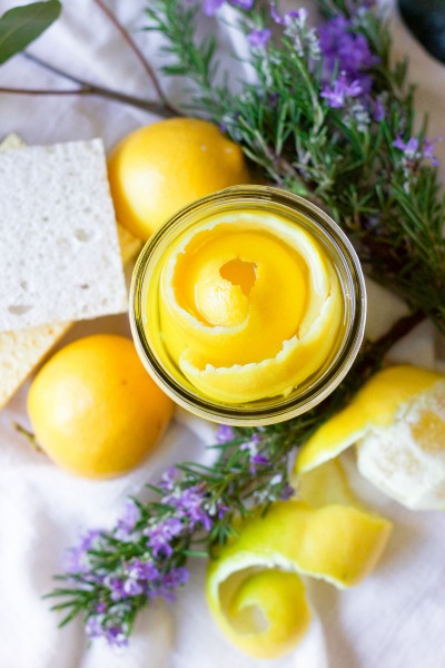 Lemon peels in a mason jar, fresh herbs, fresh lemons and kitchen dish sponges.