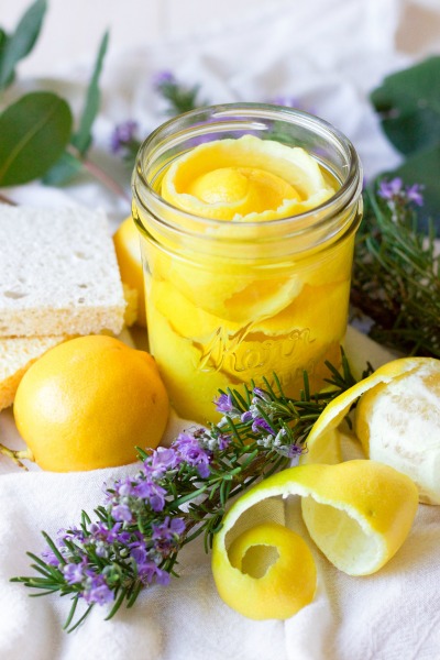 Lemon peels in a mason jar, fresh rosemary, fresh lemons and kitchen dish sponges.