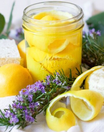 Lemon peels in a mason jar, fresh lemons, fresh rosemary, fresh leaves and kitchen dish sponges.