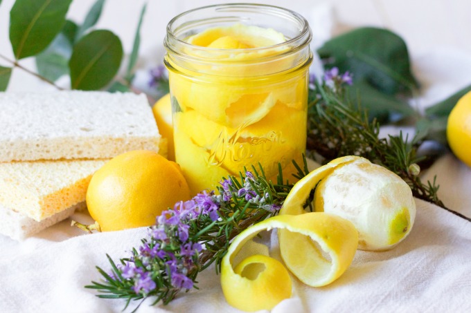 Lemon peels in a mason jar, fresh lemons, fresh rosemary, fresh leaves and kitchen dish sponges.