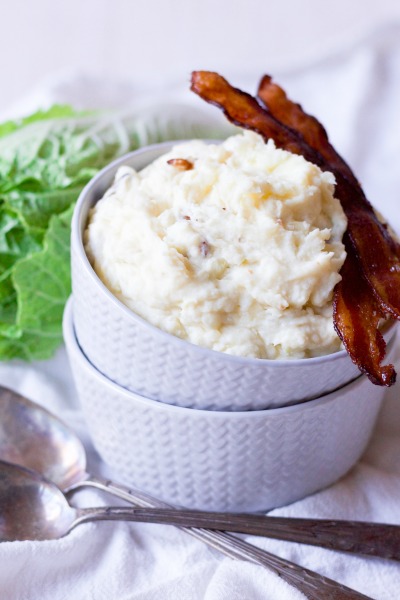Mashed potatoes in two stacked bowls with crispy bacon and green cabbage.