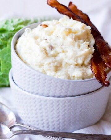 Mashed potatoes in two stacked bowls with crispy bacon and green cabbage.