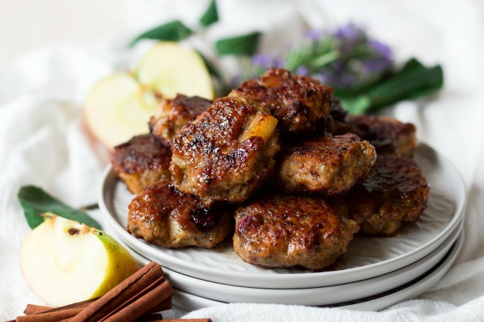 Breakfast sausage patties stacked on plates with fresh apples and cinnamon sticks.