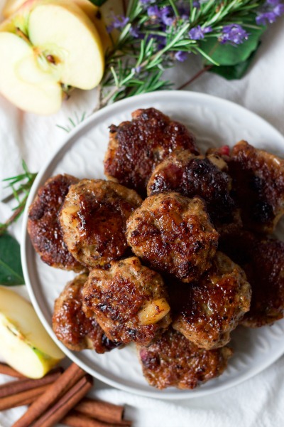 Breakfast sausage patties stacked on plates with fresh apples, cinnamon sticks and fresh rosemary.