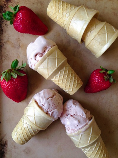 Scoops of strawberry ice cream in ice cream cones with fresh strawberries.