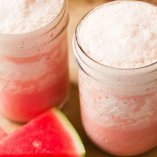 Watermelon milkshakes in 2 mason jars with fresh watermelon slices.