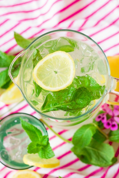 Iced mint lemonade in a pitcher and a glass with fresh lemon slices and mint.