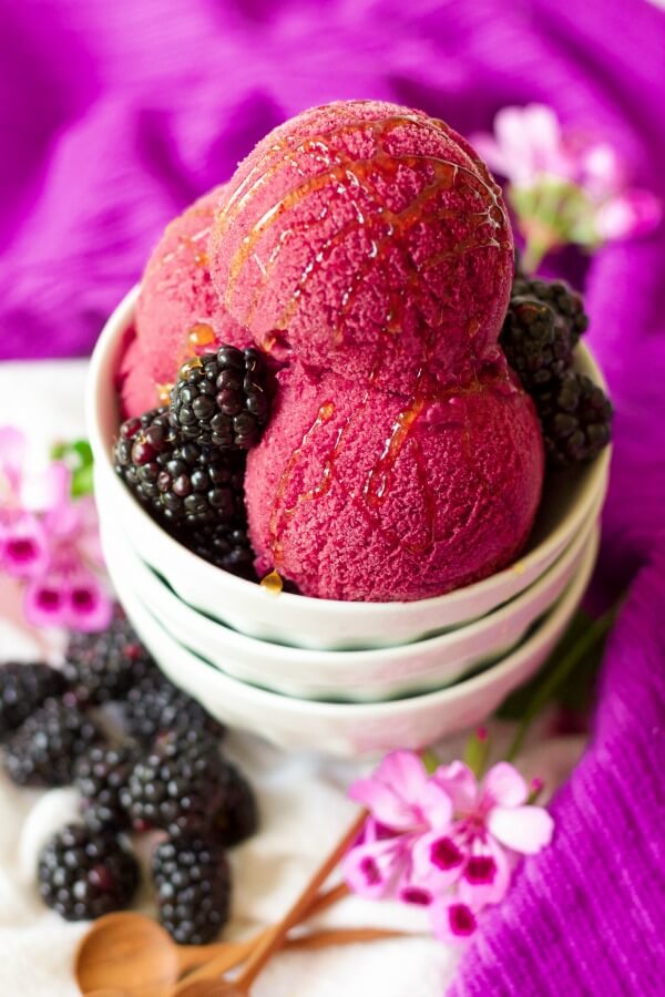 Bowl of scoops of blackberry ice cream with fresh blackberries and drizzled with honey.