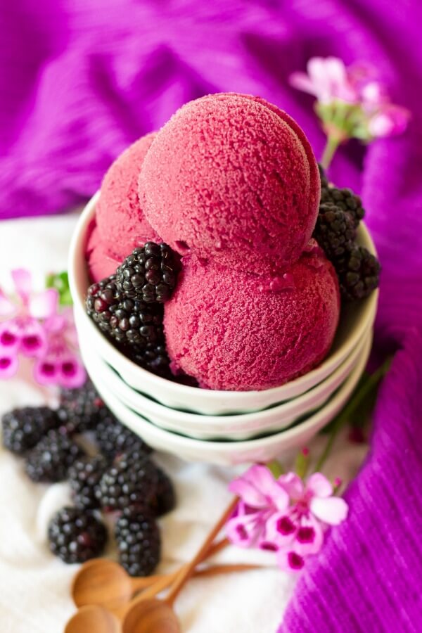 Bowl full of scoops of blackberry ice cream and fresh blackberries.