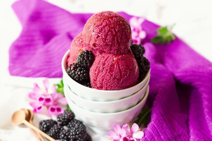Bowl full of scoops of blackberry ice cream with fresh blackberries and drizzled with honey.