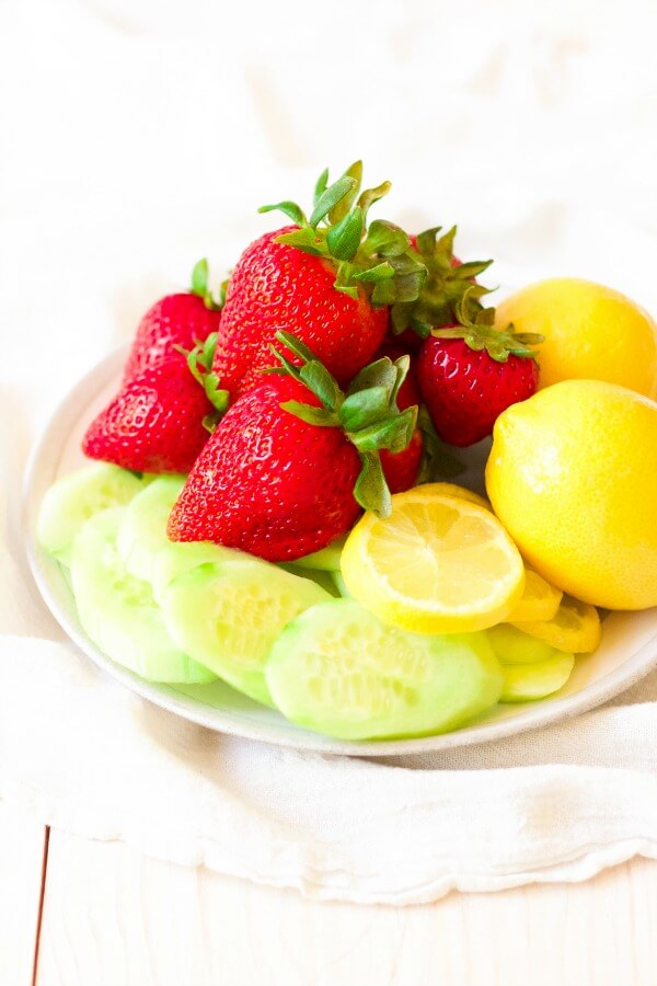 Plate full of fresh strawberries, lemons, lemon slices and cucumber slices.