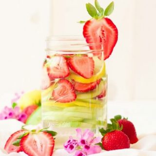 Mason jars filled with water, strawberries, lemon slices and cucumber slices.
