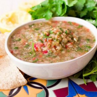 Large bowl of chunky blender salsa surrounded by chips, cilantro and juiced lemons.