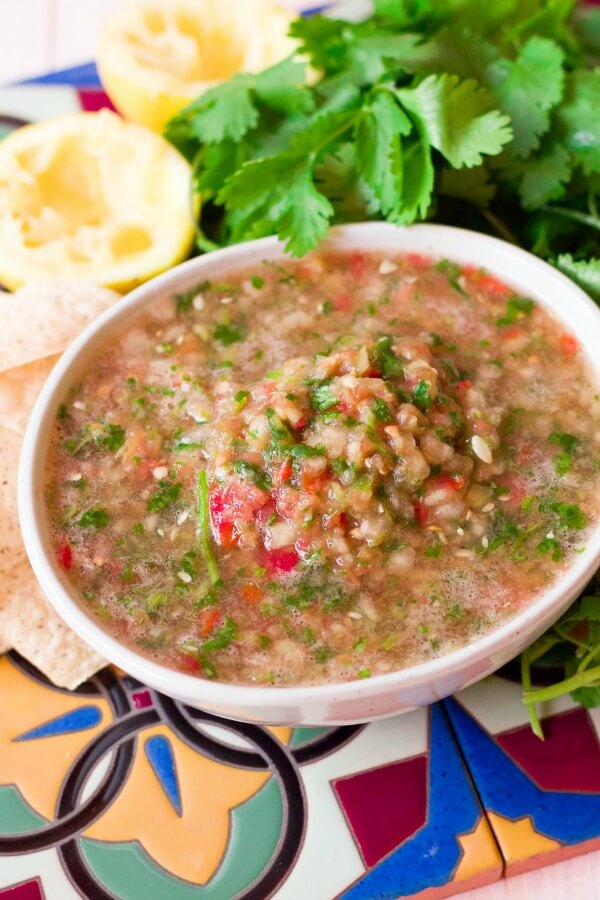 Large bowl of chunky blender salsa surrounded by chips, cilantro and juiced lemons.