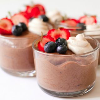 Jars of smooth chocolate chia pudding with berries and cream on the top.